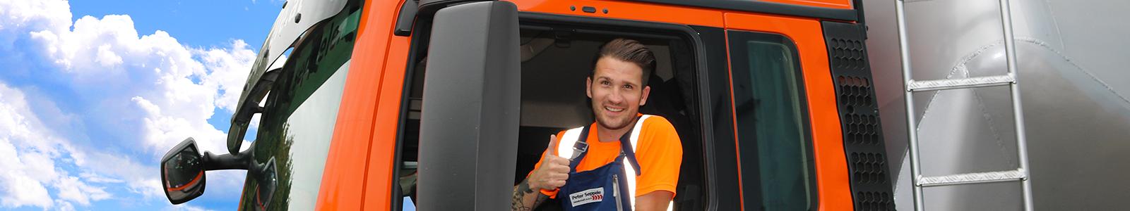 Ein freundlicher Lkw-Fahrer zeigt einen Daumen hoch aus seinem Lastwagenkabinenfenster. Der orangefarbene Lkw ist auf einer malerischen Strecke mit strahlend blauem Himmel unterwegs. Im Hintergrund sind grüne Wiesen und Berge zu sehen, was eine einladende Atmosphäre schafft.
